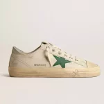 Sneakers Golden Goose dotées d’une tige en cuir brillant blanc cassé, ce modèle se distingue par une étoile en cuir vert. Les lacets beiges apportent la touche finale.